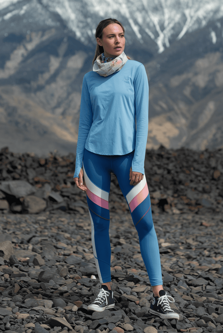 Young woman in athletic wear stands on rocky terrain with snow-capped mountains in background.