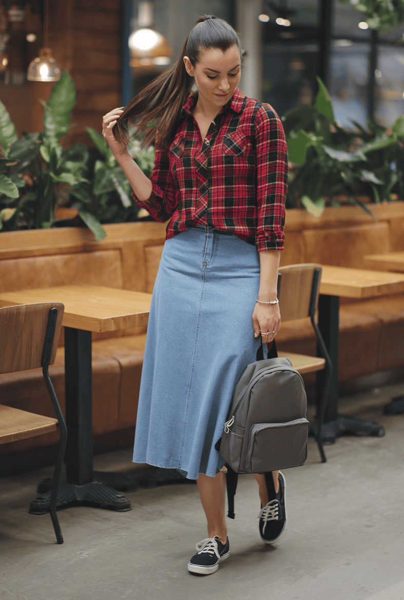 Young woman in stylish plaid shirt and denim skirt in modern cafe setting.