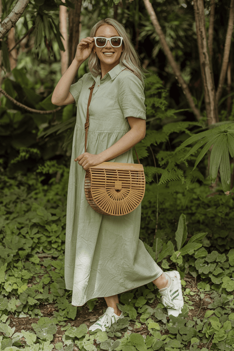 Young woman in a tropical dress smiles among lush greenery, showcasing eco-friendly fashion.