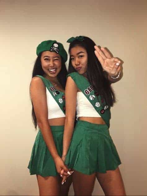 Two young women in matching green costumes pose playfully at a themed party, celebrating friendship.
