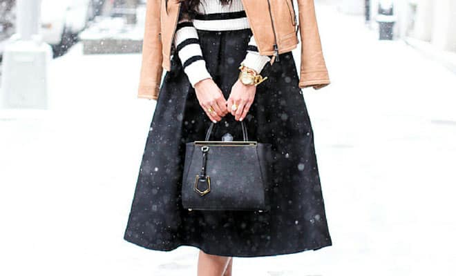 Chic winter outfit with black midi skirt, striped top, leather jacket, gold watch, and black handbag.