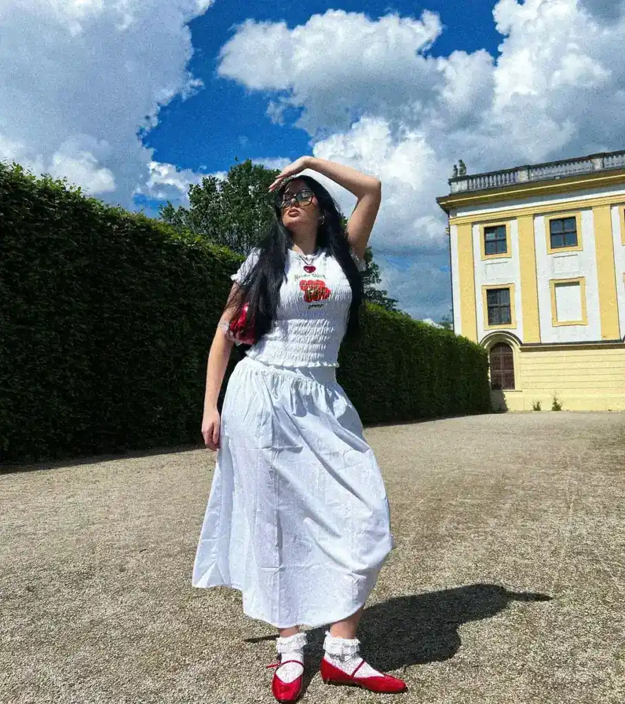 feminine outfit idea with a white graphic tee, long blue midi skirt and red ballet shoes