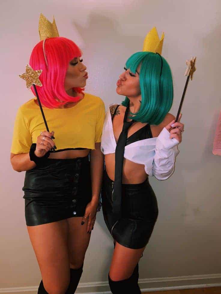 Two friends in colorful wigs and playful outfits pose with star wands at a party.