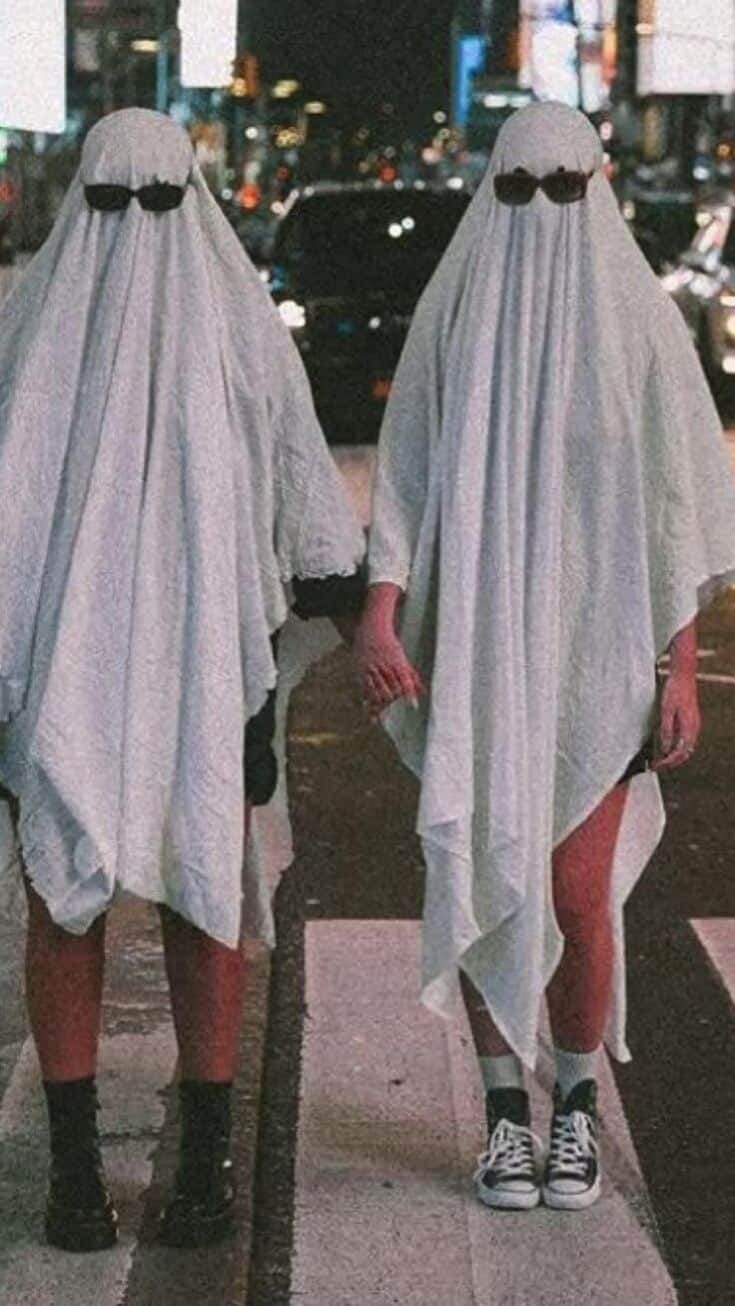 Two people in ghost costumes crossing a city street at night, urban nightlife Halloween photo.