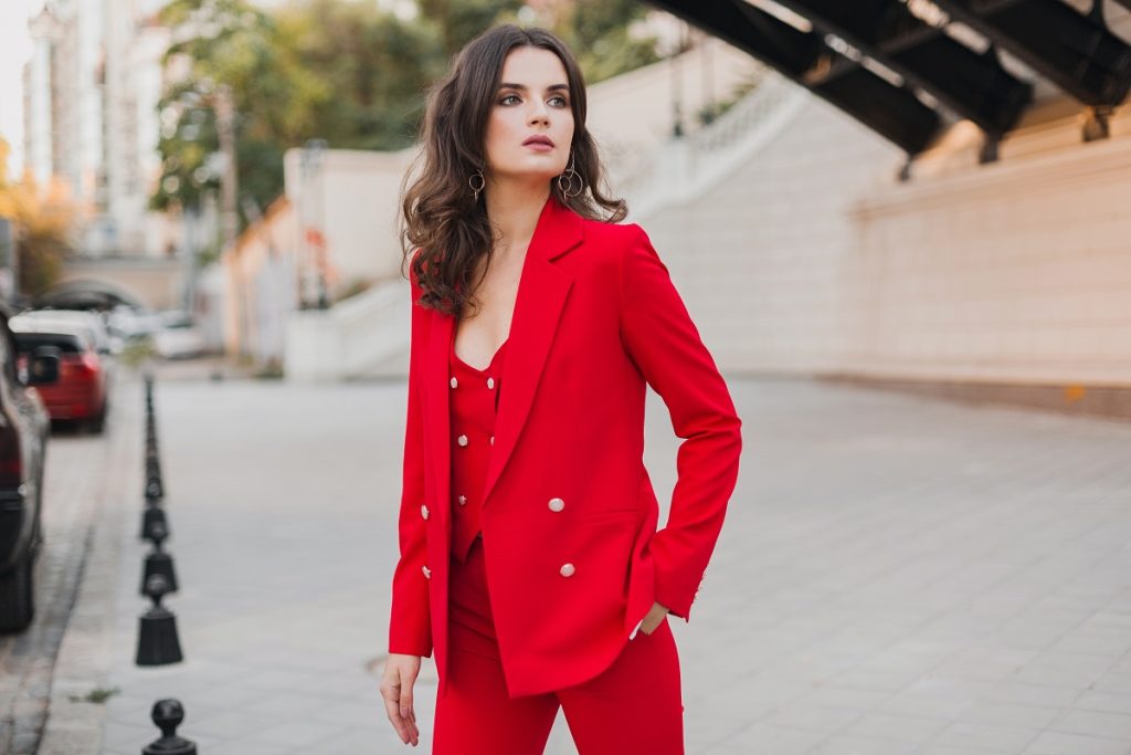 Confident businesswoman in a red suit posing stylishly on a city street in summer.