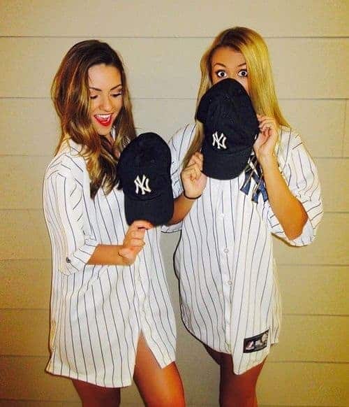 Two college girls in Yankees baseball costumes posing playfully, perfect best friend Halloween outfit idea.