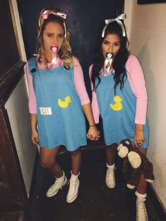 Two college girls in matching baby-themed costumes pose for a fun Halloween party photo.