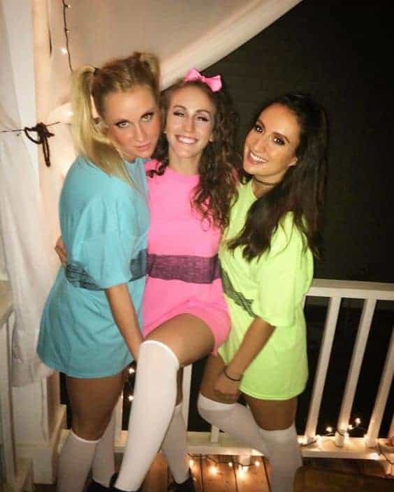 Three college girls in colorful oversized t-shirts pose on a porch for a fun Halloween photo.