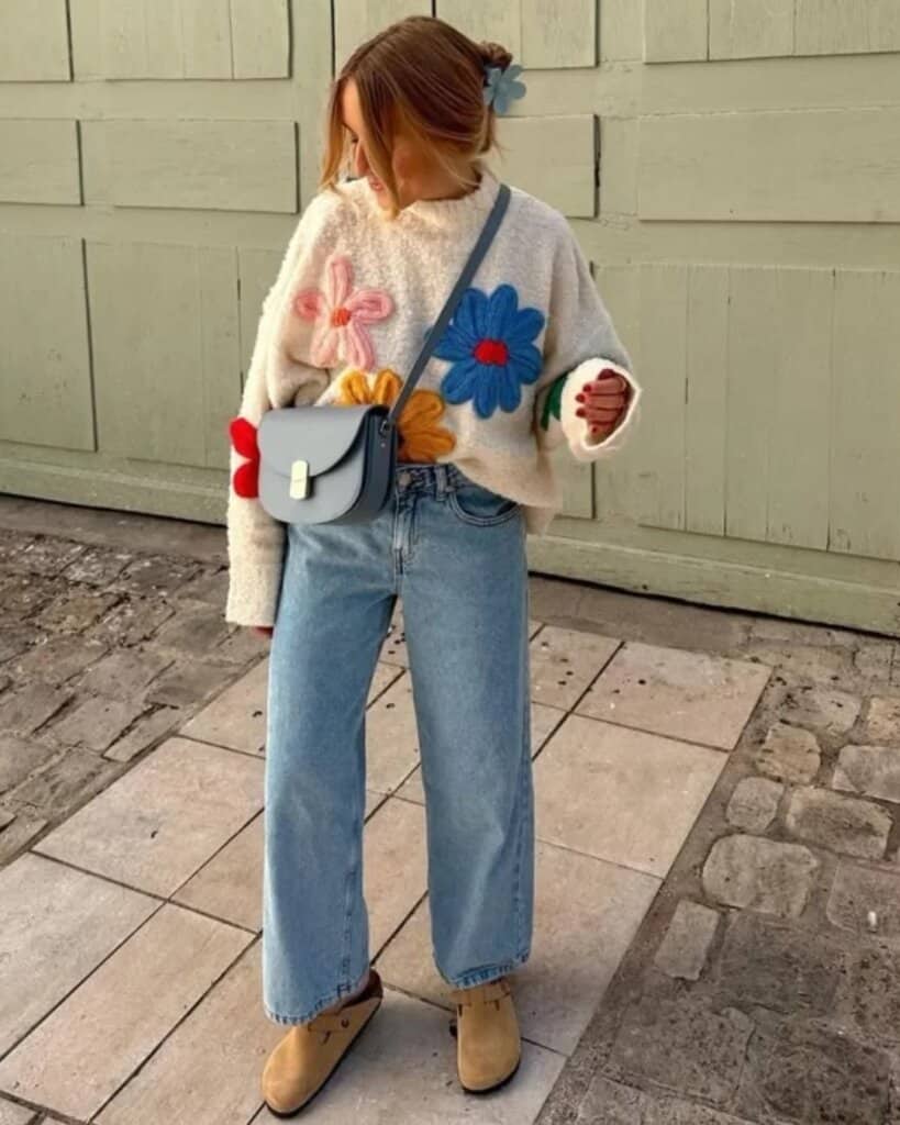 Woman in floral embroidered sweater, high-waisted jeans, and ankle boots, casual spring street style.