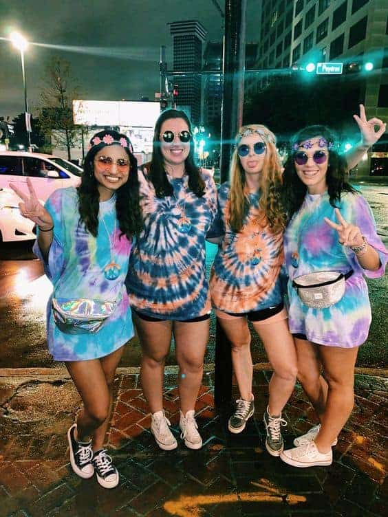 Group of friends in tie-dye shirts posing on a city street at night, smiling and stylish.
