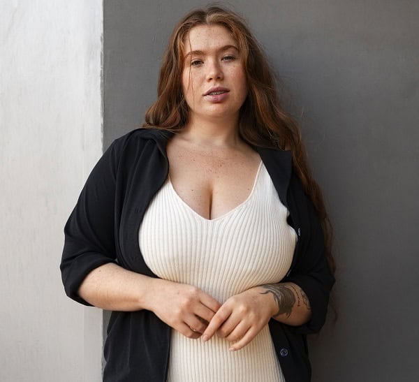 Confident plus-size woman in trendy white dress and black shirt against modern grey background.