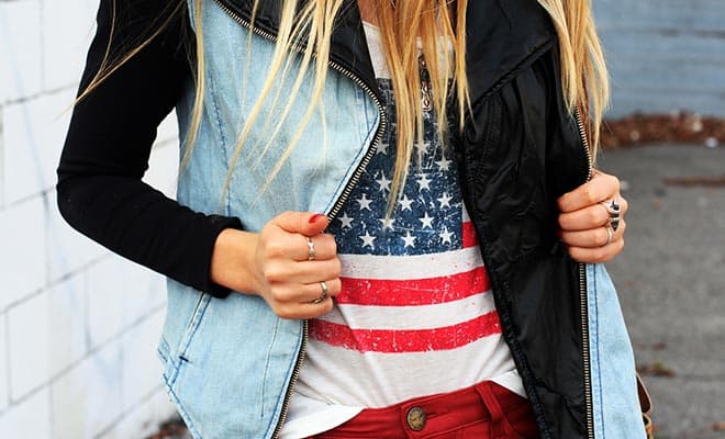 Trendy woman in denim vest, American flag shirt, and red pants in urban setting.