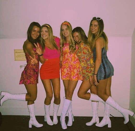 Group of friends in 1960s retro Halloween costumes posing together in colorful dresses and boots.