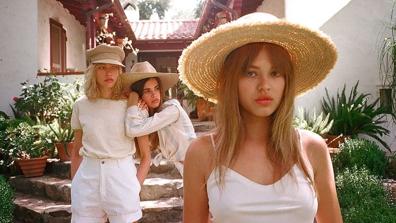 Three stylish young women in summer hats enjoying a sunny garden gathering outdoors.
