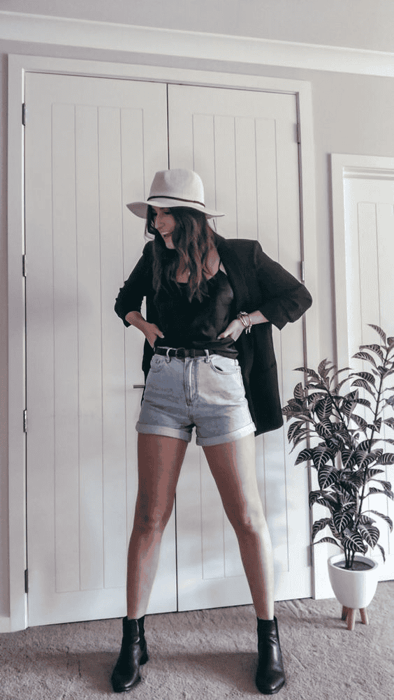 Stylish woman in summer outfit with blazer and hat poses indoors near white doors and potted plant.