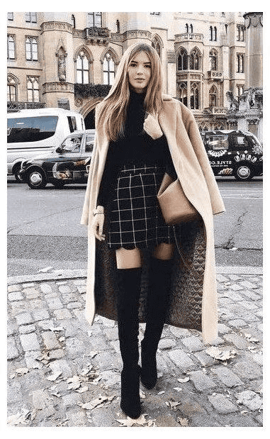 Stylish woman in plaid skirt and thigh-high boots on elegant urban street with historic architecture.