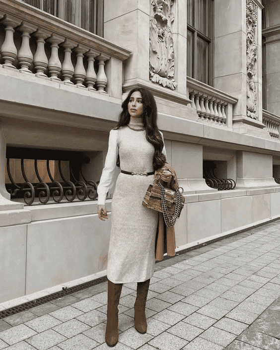 Fashionable woman in layered dress and boots posing by elegant urban stone architecture.