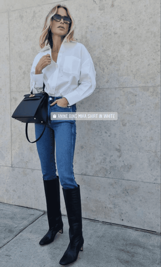 Chic woman in white shirt, denim jeans, and black knee-high boots posing stylishly outdoors.