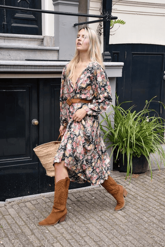 Young woman in floral dress and boots walks on cobblestone street with a straw basket.