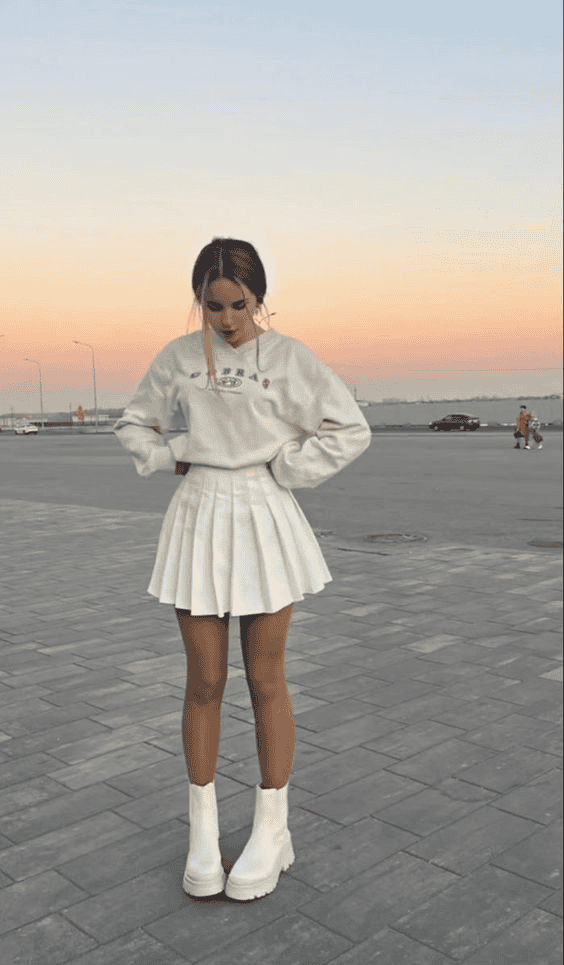 Trendy woman in white sweatshirt and mini skirt posing at sunset in urban street style.