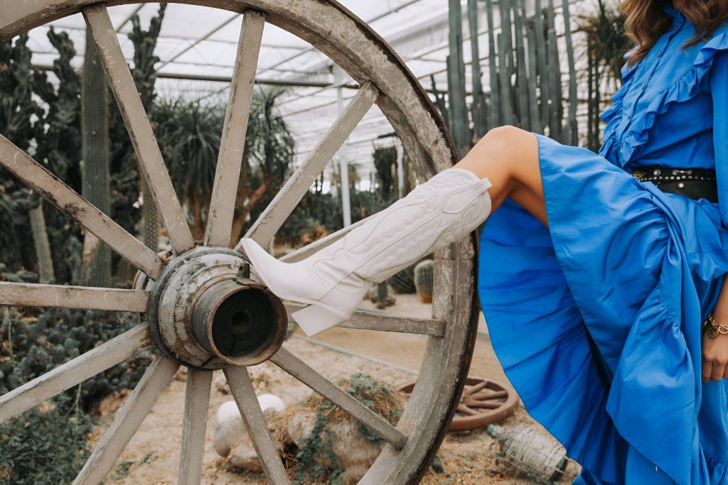 White cowboy boot and blue ruffled dress by rustic wagon wheel in cactus greenhouse.