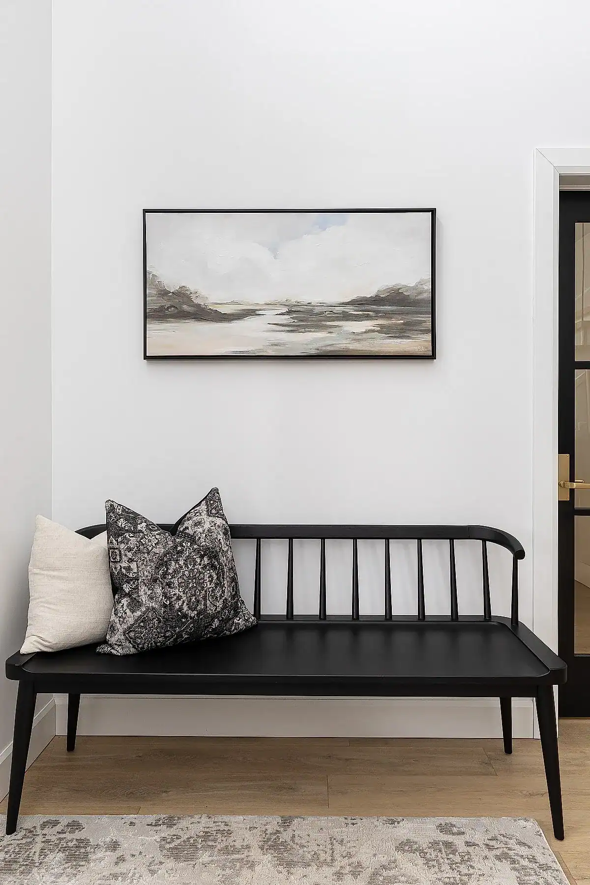 Entryway featuring a black bench with decorative pillows, minimalist artwork, and light wood flooring.