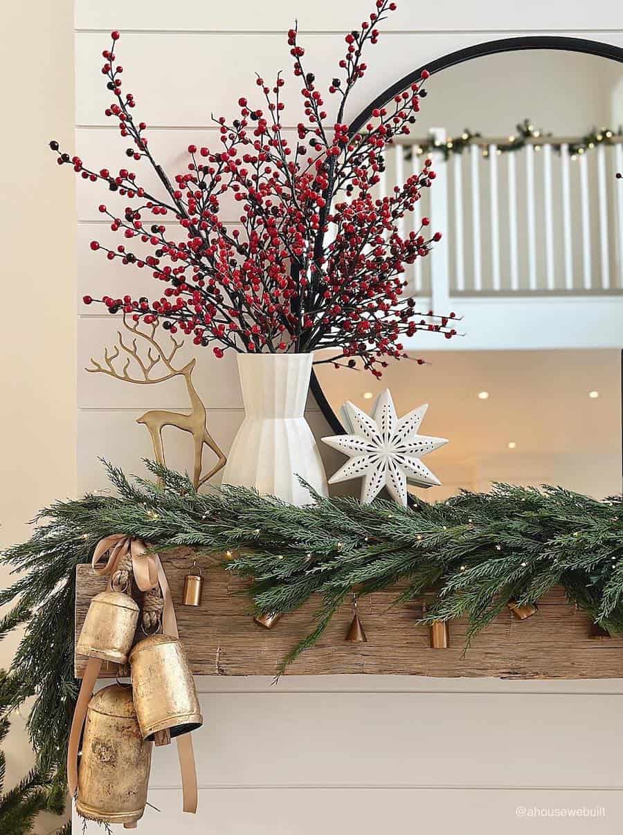 a mantle with holly berries, reindeer decor, bells, and pine garland
