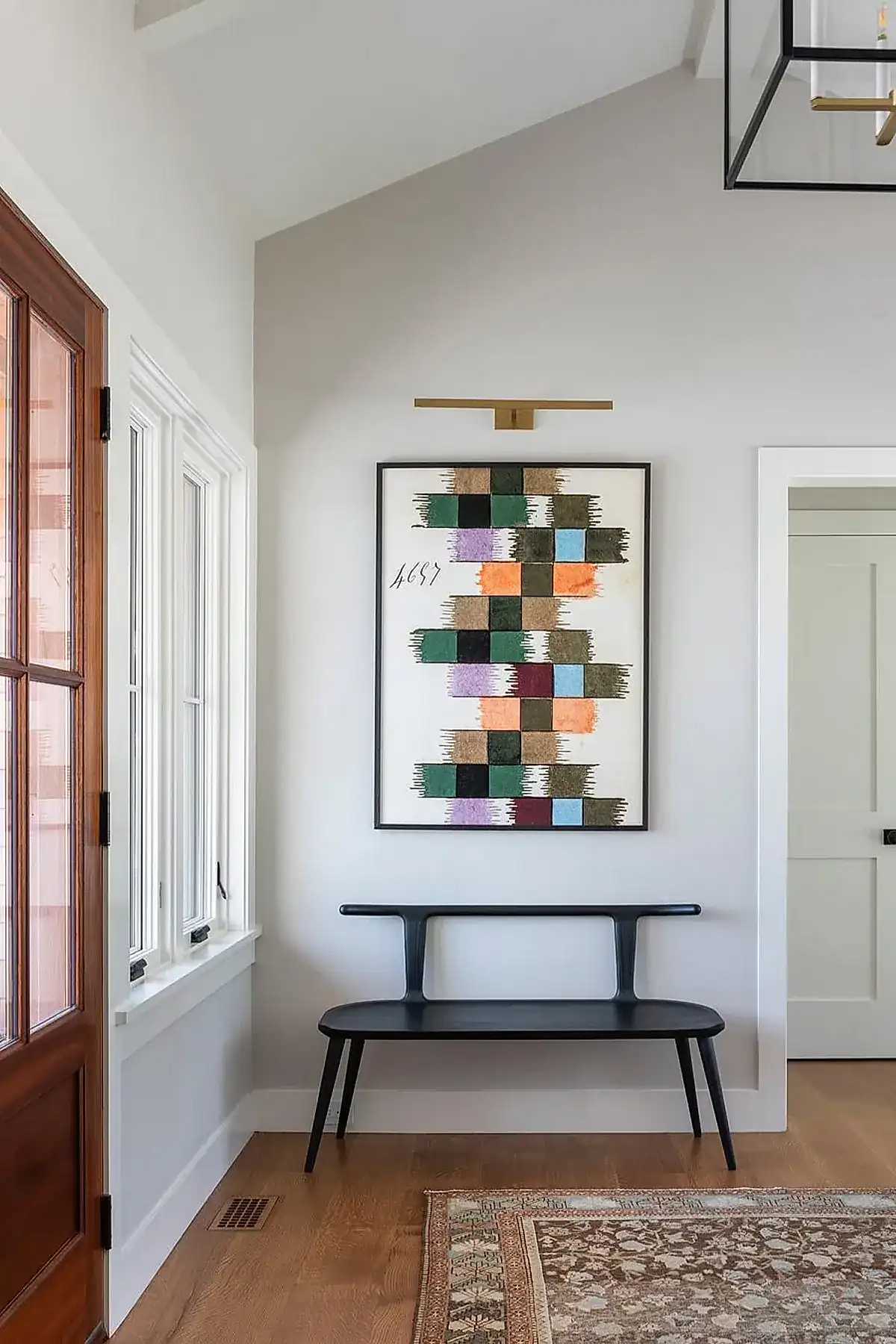 Modern entryway featuring a black bench and colorful geometric artwork on the wall.