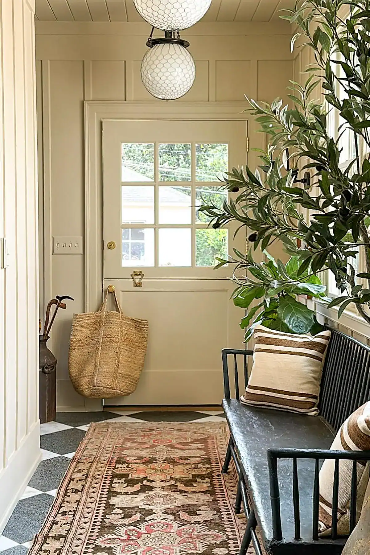 Entryway with black bench, striped pillows, decorative rug, and plants near the door.