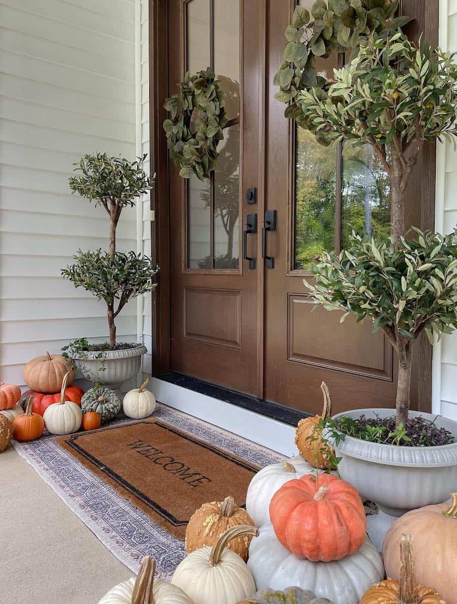 a front porch with piles of pumpkins and plants