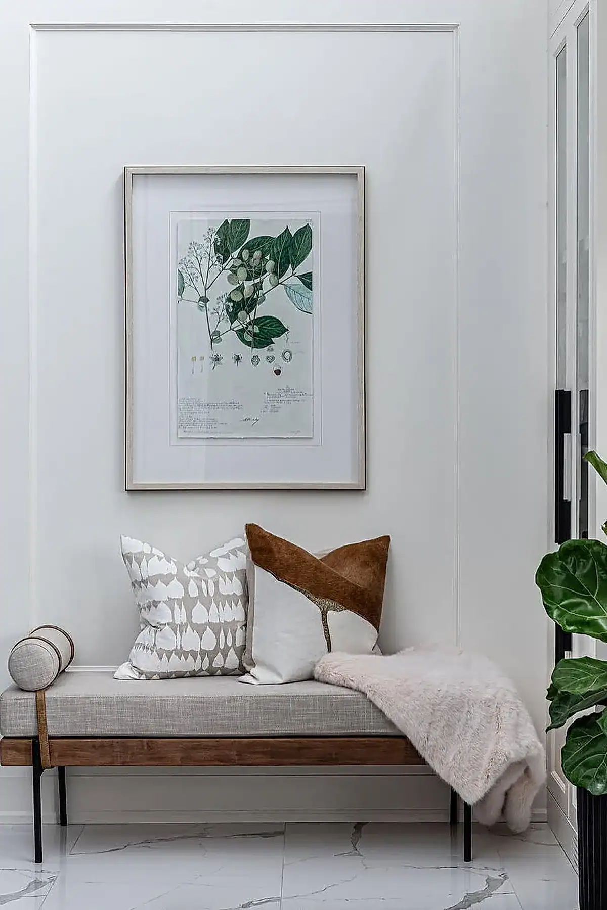 Entryway featuring a wooden bench with decorative pillows, botanical artwork, and marble flooring.
