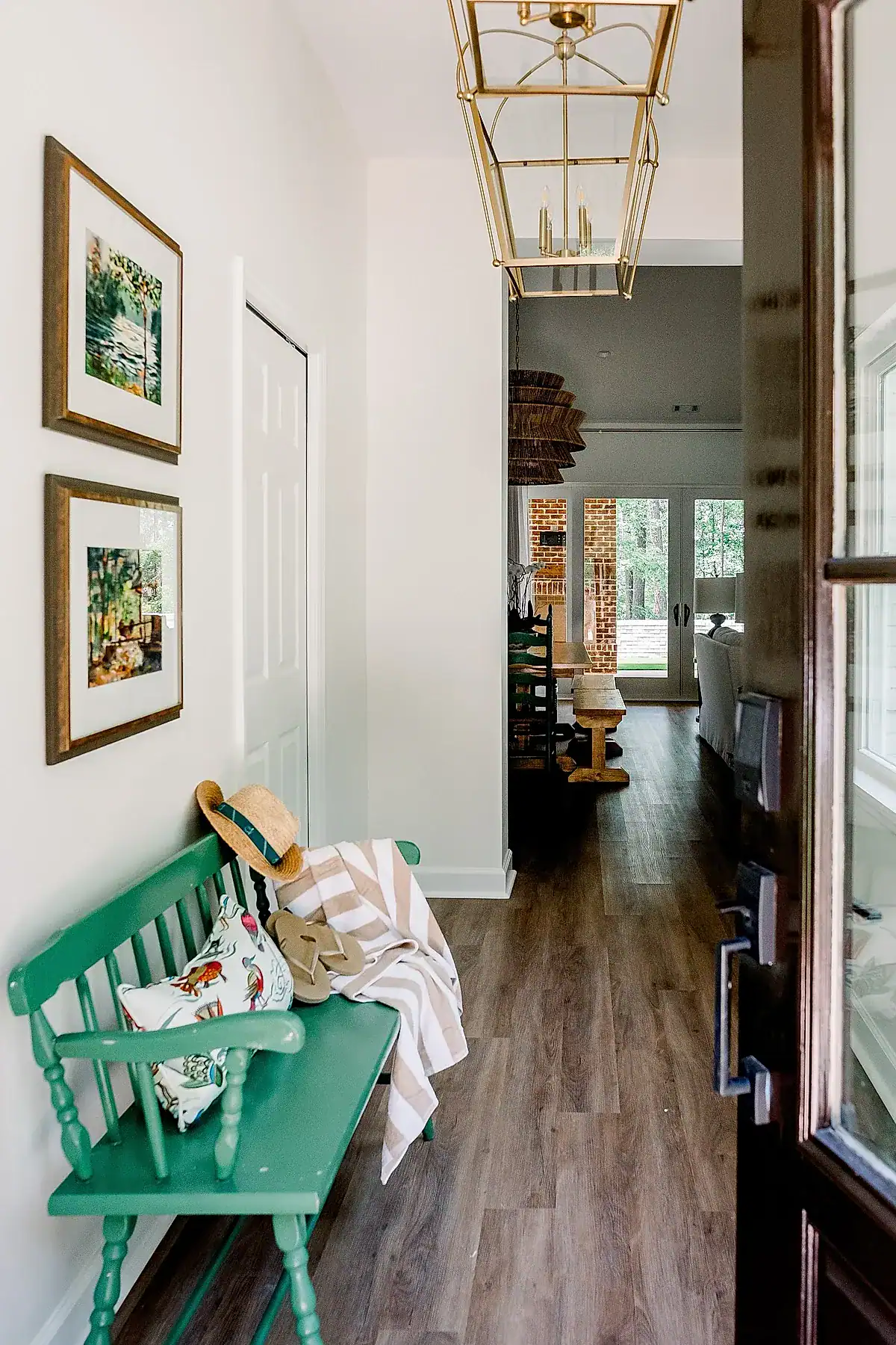 Entryway featuring a green wooden bench with floral pillow and wall art on white walls.