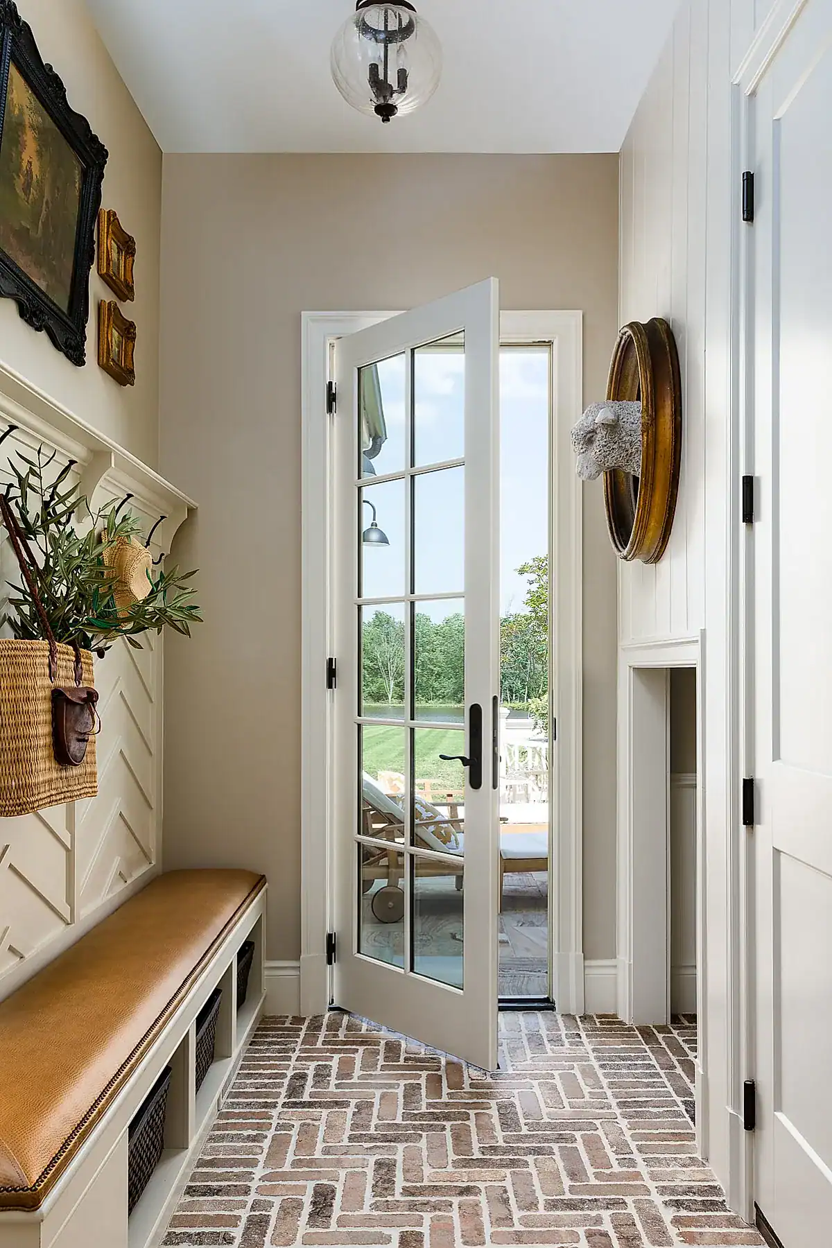 Entryway with a leather-cushioned bench, herringbone brick floor, wall hooks, and classic wall art.