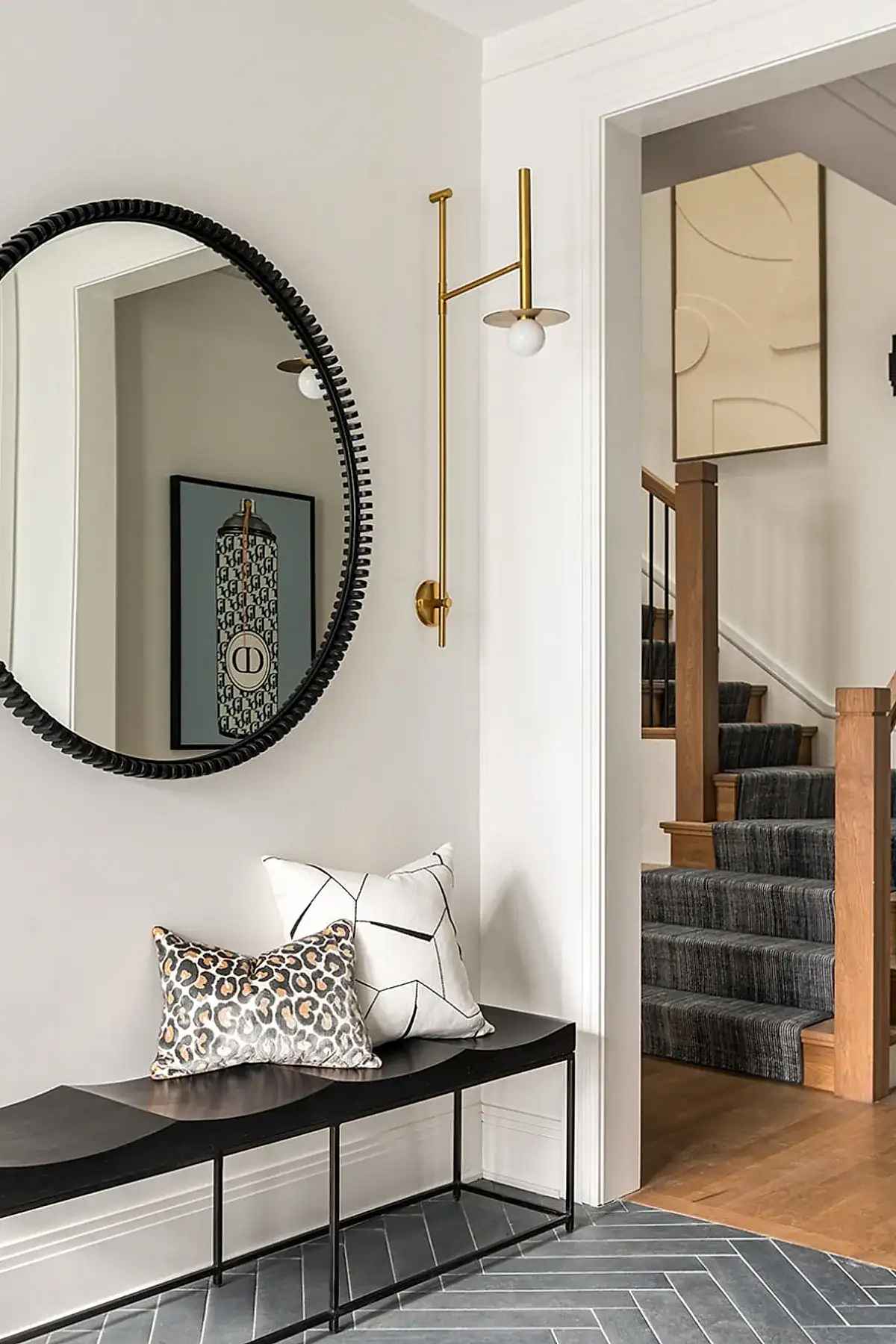 Modern entryway featuring a black bench with decorative pillows, round mirror, and unique wall light.
