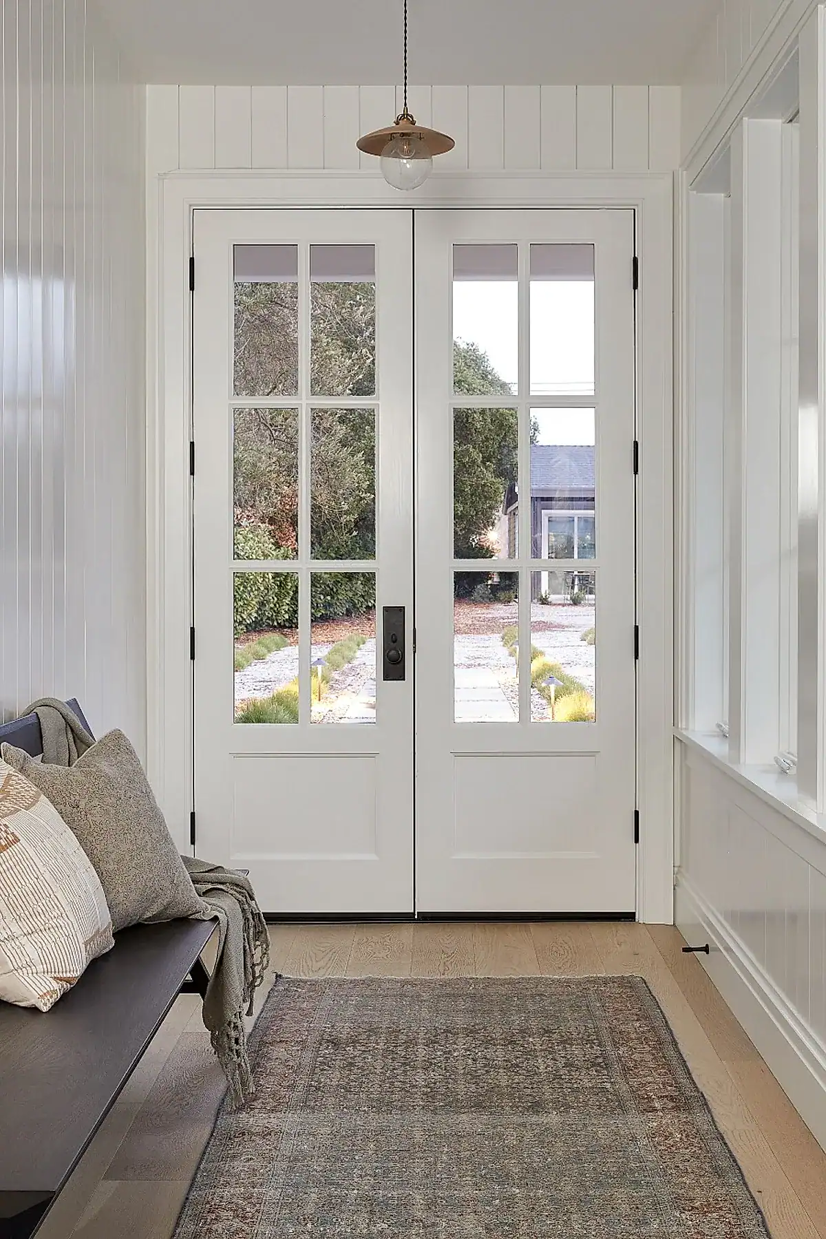 Entryway with a black bench, textured rug, white paneling, and large glass doors.