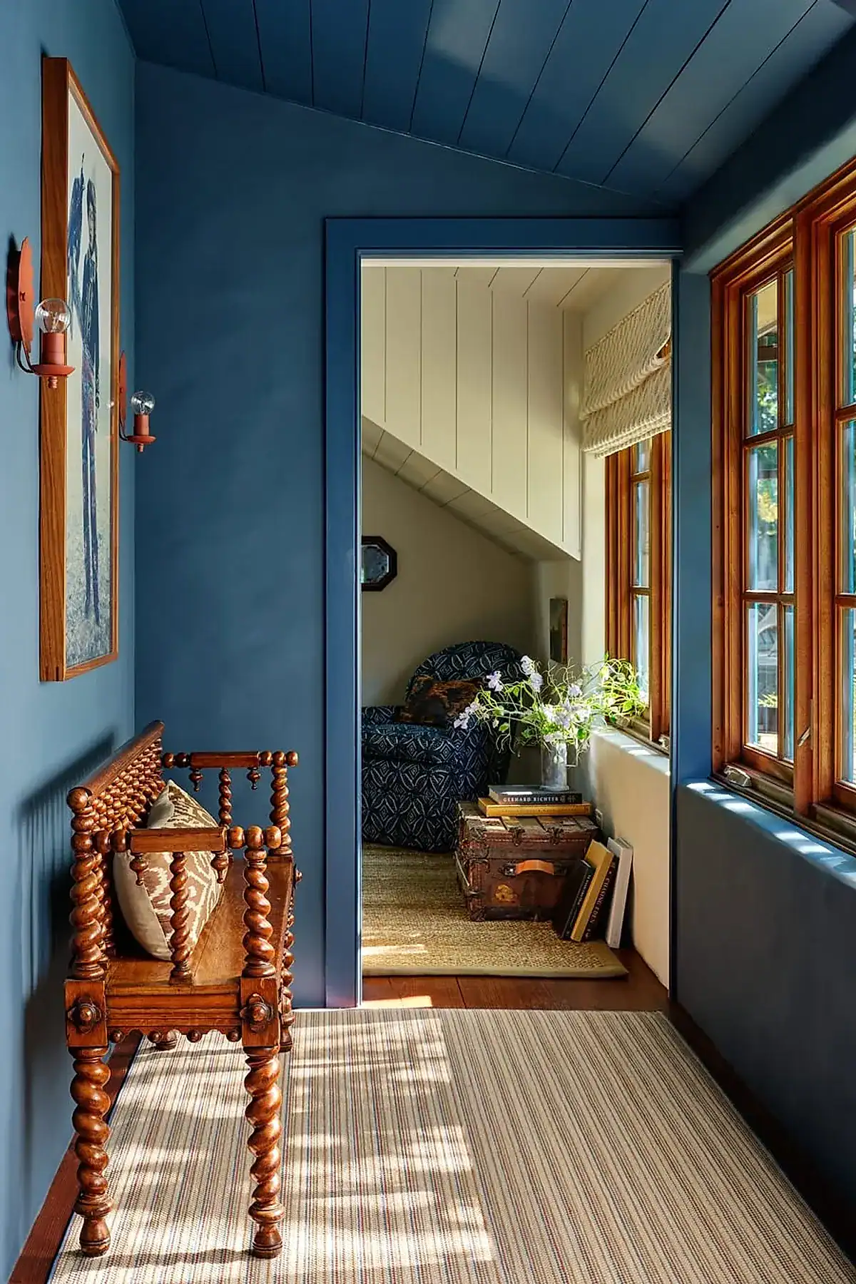 Antique wooden bench with carved details in a blue-walled entryway with striped rug and wall decor.