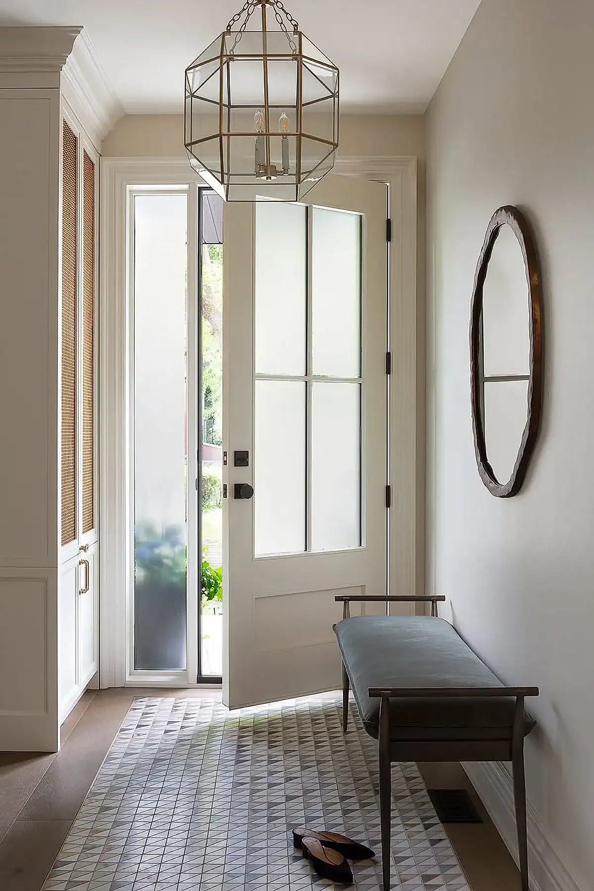 Entryway featuring a modern bench with cushion, geometric floor tiles, pendant light, and an open front door.