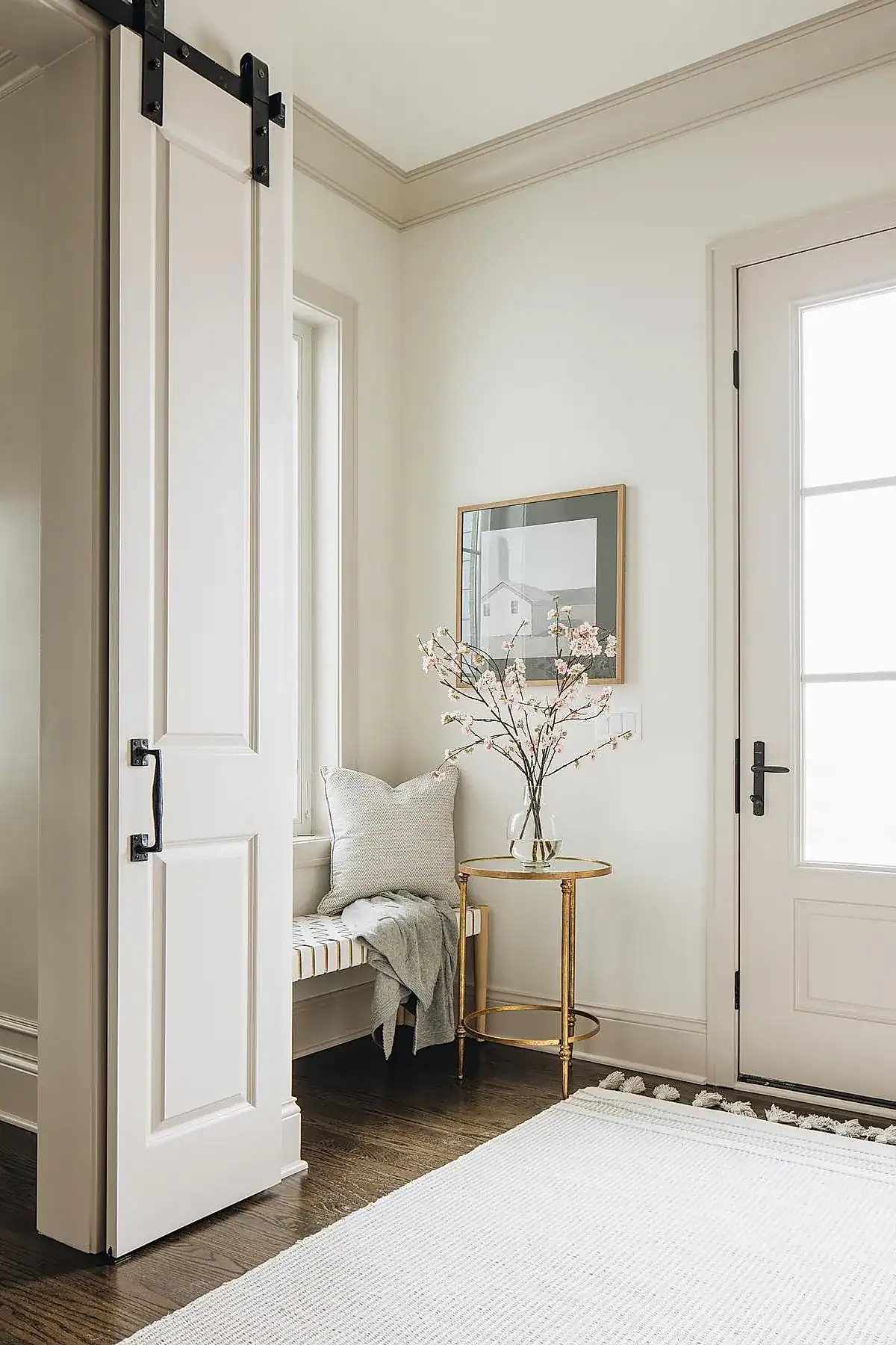 White entryway featuring a built-in bench with a striped cushion, gold side table with flowers, and framed artwork.